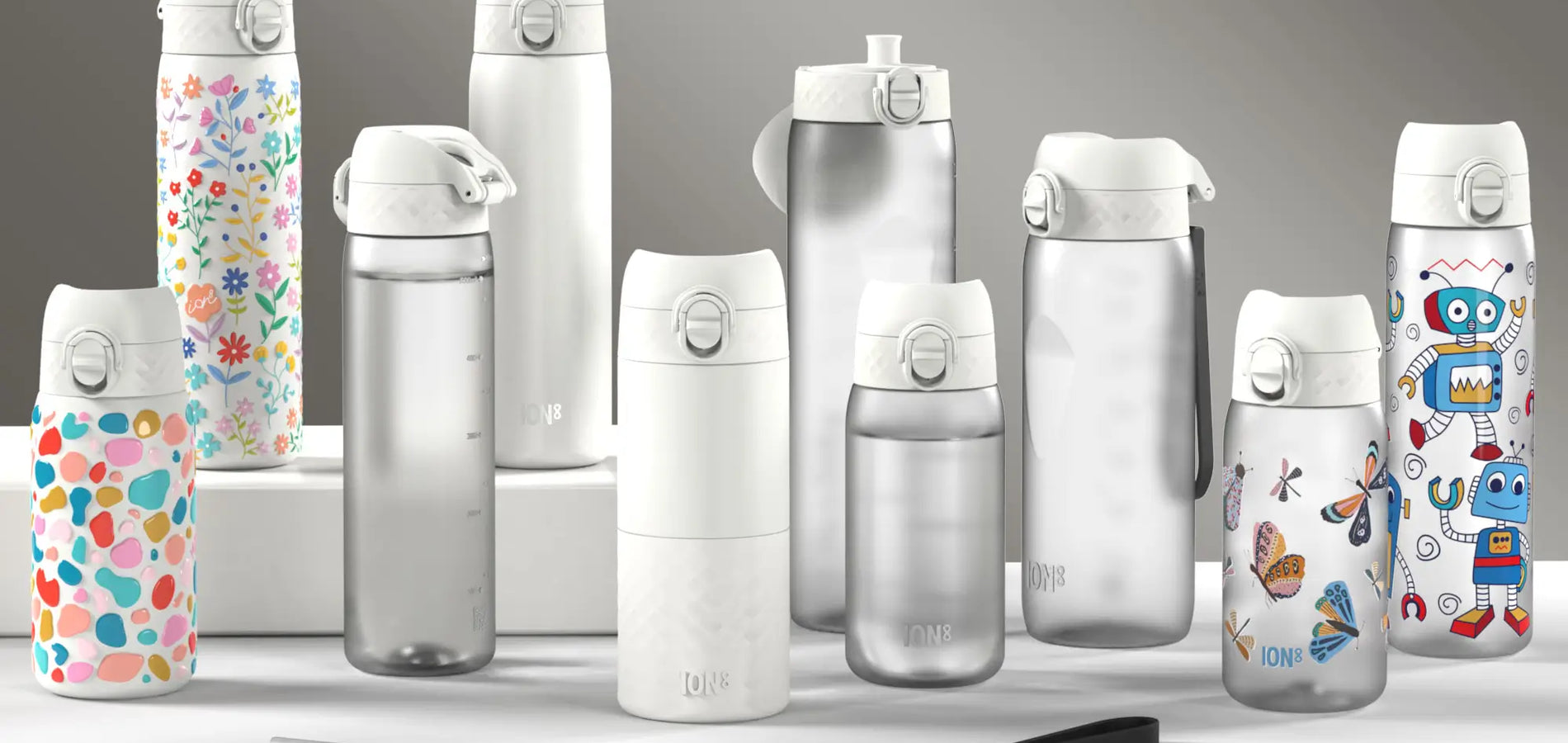 Several ION8 water bottles of varying designs and sizes are displayed on a white surface against a gray background. A straw is also present.
