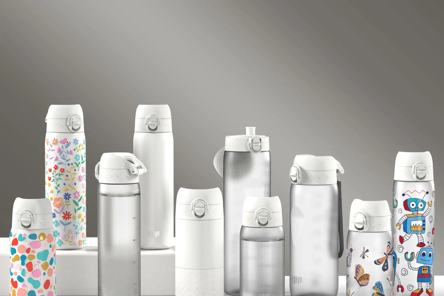 Several ION8 water bottles, displaying various designs and sizes, sit on a white surface against a gray backdrop. A cleaning straw is also present.