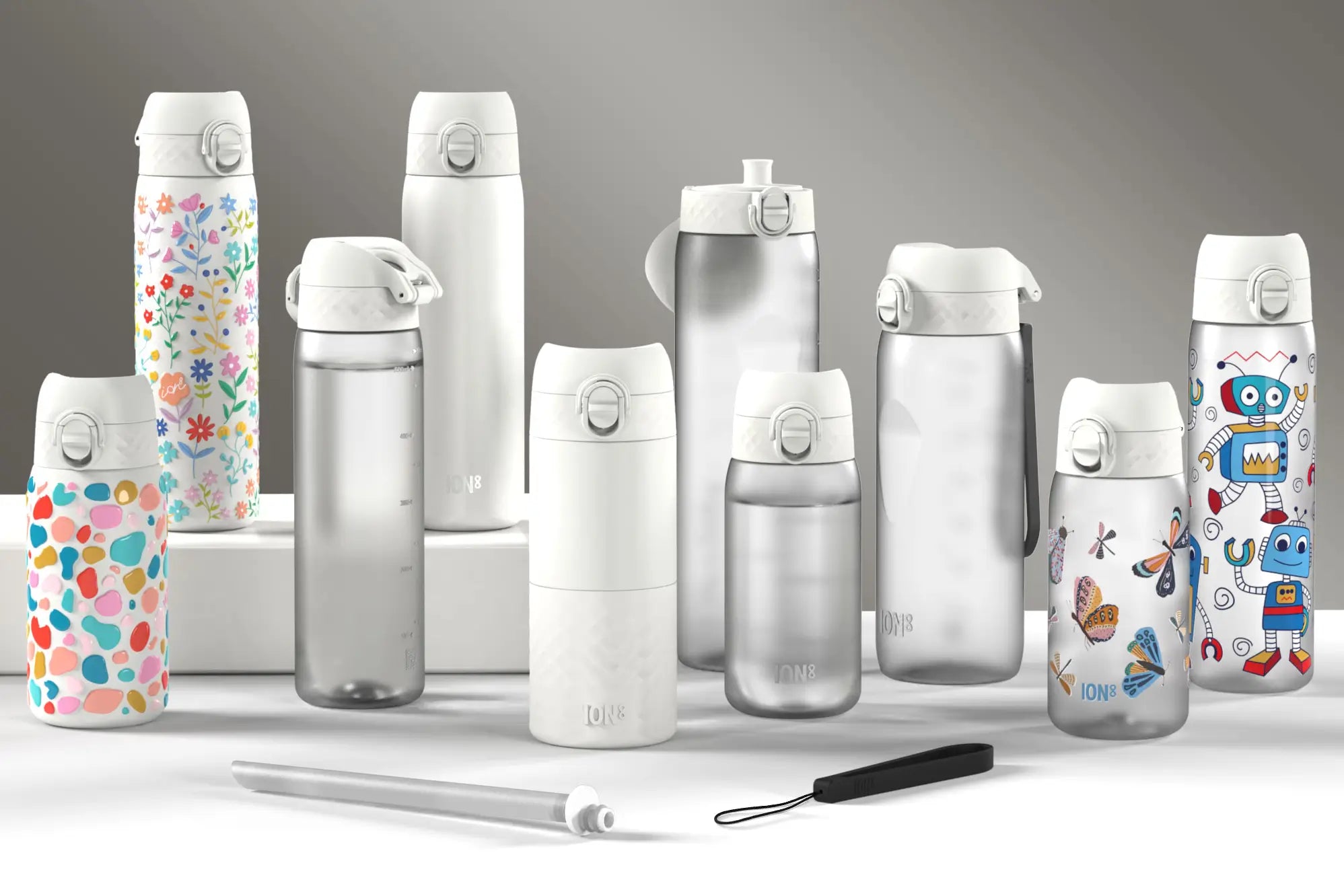 Several ION8 water bottles of varying designs and sizes are displayed on a white surface against a gray background. A straw is also present.