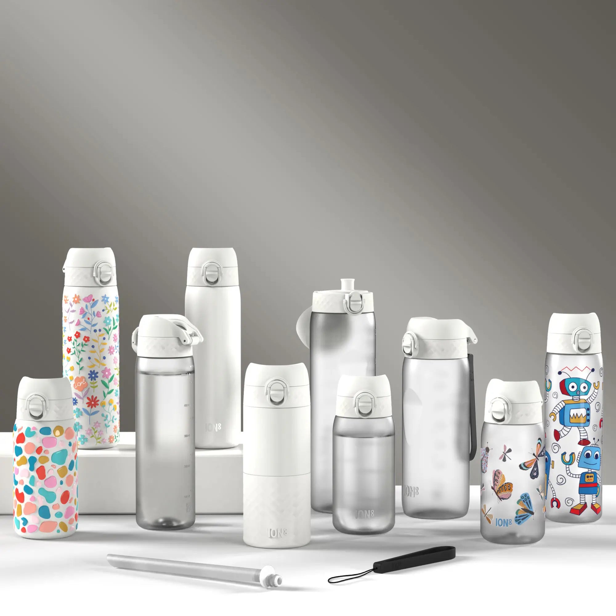Several ION8 water bottles, displaying various designs and sizes, sit on a white surface against a gray backdrop. A cleaning straw is also present.