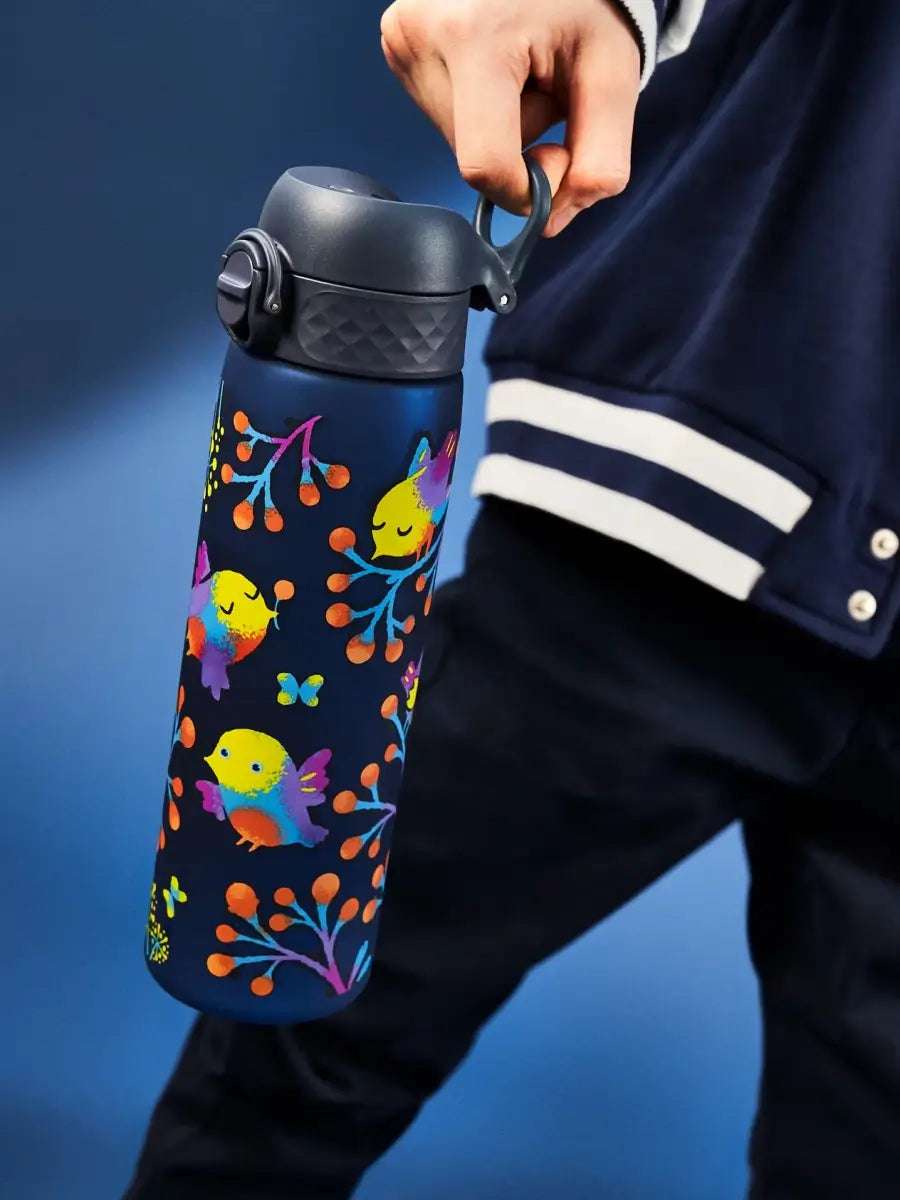 A dark-blue water bottle, decorated with colorful birds and floral designs, is held by a person against a blue background.