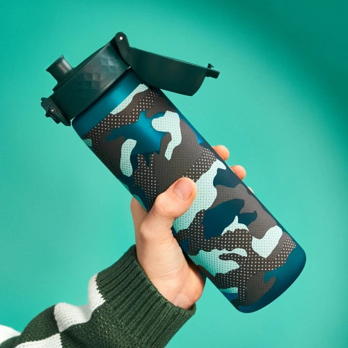 A camouflage-patterned water bottle is being held; a person’s hand grips it against a teal backdrop.