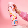 A pink water bottle, adorned with rainbow and sun designs, is being held by a person against a pink background.