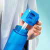 A blue water bottle has a blue cap with a straw being inserted by a person wearing a white robe.